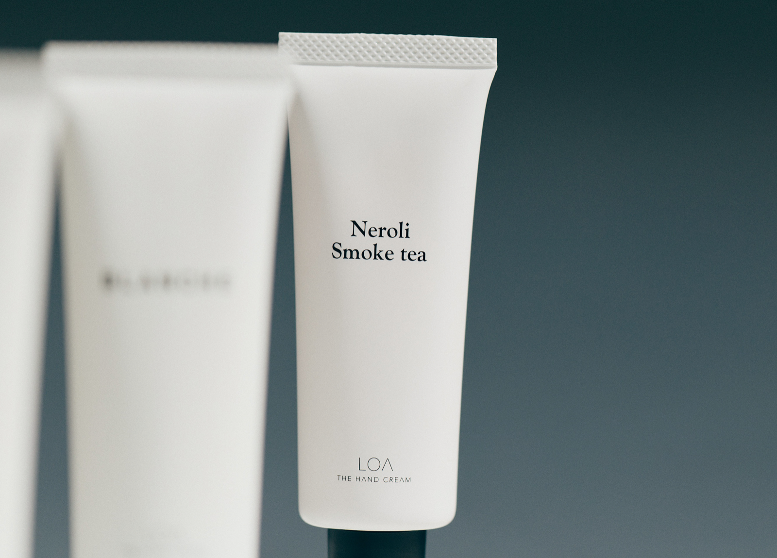 Jade Japan公式配布のNeroli Smoke teaのハンドクリーム写真。前景のチューブに香り名とTHE HAND CREAMの表記が見える同版画像。背景に写る別香調の容器を購入対象と混同しないようにします。