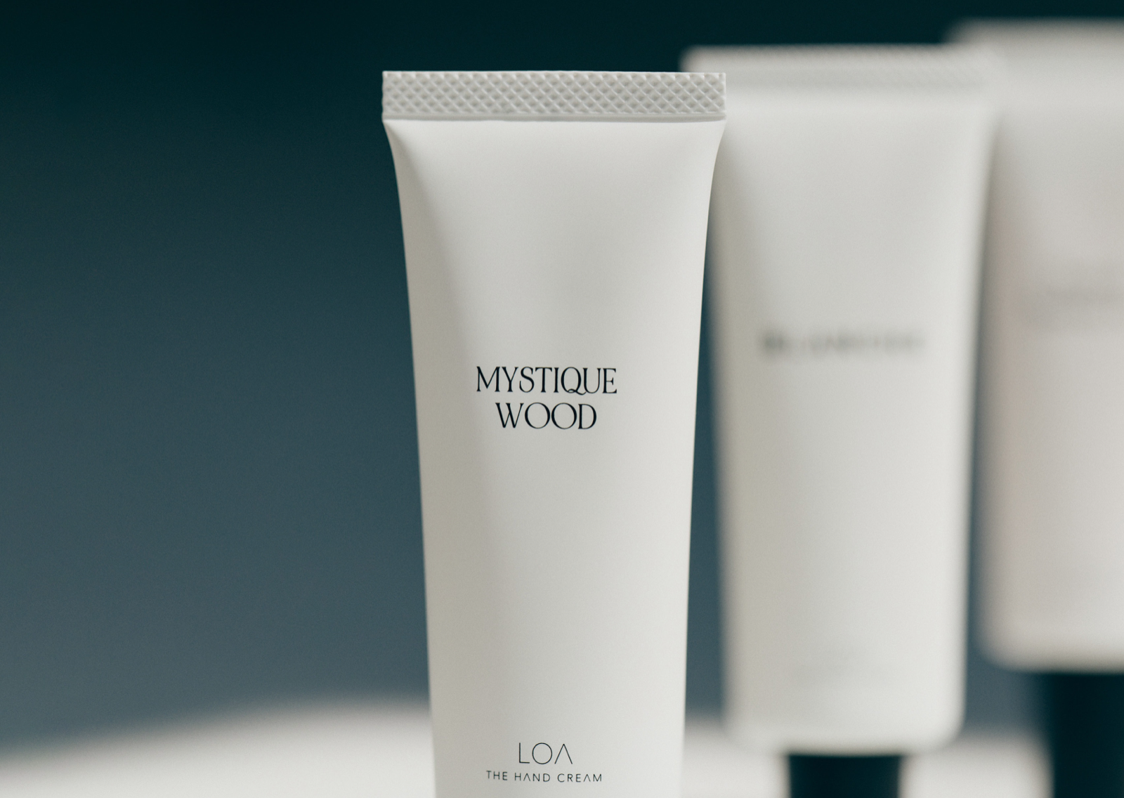 Jade Japan公式配布のMYSTIQUE WOODのハンドクリーム写真。前景のチューブに香り名とTHE HAND CREAMの表記が見える同版画像。背景に写る別香調の容器を購入対象と混同しないようにします。